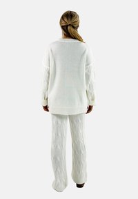Maglione bianco lavorato a maglia con maniche a treccia, abbinato a pantaloni coordinati a treccia. Dettaglio a costina sui polsini e sull'orlo. Tessuto morbido e dalla texture particolare.