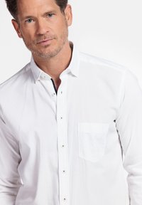 Witte button-up shirt van lichtgewicht stof, met een borstzak, subtiele textuur en kleine zilveren knopen aan de voorkant.