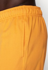 Oranžid dressipüksid elastse vöökoha ja küljetaskuga, valmistatud pehmest, tekstureeritud kangast mugavuse tagamiseks.