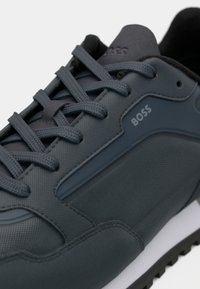 Mørkegrå sneakers med teksturert stoff, glatte detaljer og en kontrasterende hvit mellomsole. Snøring med BOSS-logo.