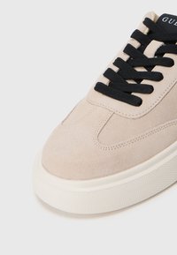 Beige semsket sneaker med rund tå, sorte snørebånd og en teksturert gummisåle. Har subtil søm og en logoetikett på tungen.