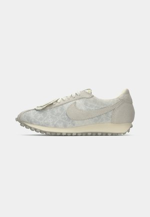Sneaker beige a profilo basso con sovrapposizioni in suede, suola testurizzata, chiusura con lacci e una tomaia in tessuto con un motivo sottile.