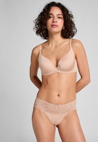 Nude beha met gladde, gevormde cups en verstelbare bandjes; gecombineerd met bijpassende nude slipjes met een kanten tailleband en strikdetail.