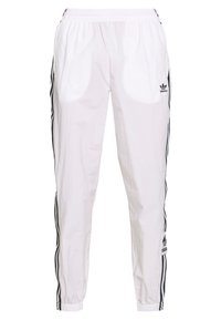 Pantalon de sport blanc avec taille élastique, présentant des bandes latérales noires et un logo brodé sur la jambe gauche. Matière légère.