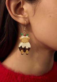 Ørering formet som en ko iført en julepudding-kostume med misteltenblade hængende fra venstre øre på en person i en rød sweater.