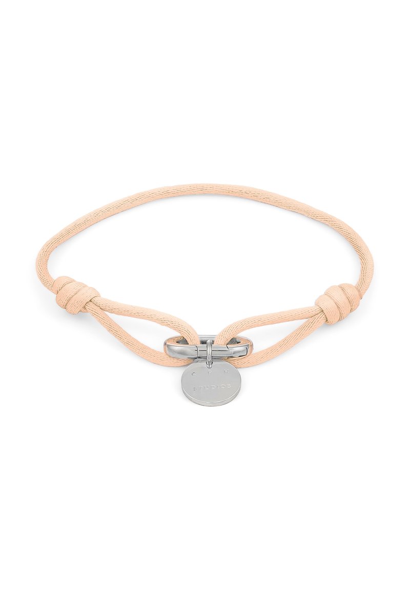 Braccialetto in tessuto color nudo con una chiusura in argento liscia e una targhetta rotonda in metallo con testo in rilievo. Presenta un design annodato per la regolazione.
