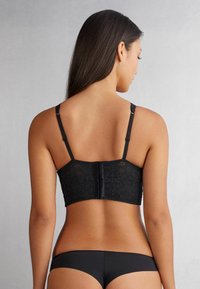 Schwarzer Spitzen-Bralette mit verstellbaren Trägern und einem Haken- und Ösenverschluss. Verfügt über eine gemusterte Spitzenoberfläche und ein glattes Unterband.