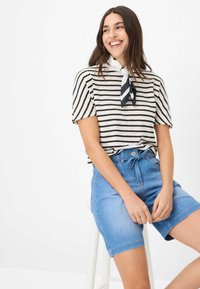 Chemise à rayures à manches courtes en beige et noir, associée à un short en denim bleu clair, avec une écharpe noire et blanche nouée autour du cou.