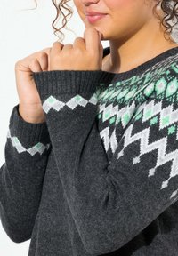 Maglione grigio lavorato a maglia con motivi geometrici bianchi e verdi sullo scollo. Presenta polsini a costine e una consistenza morbida.