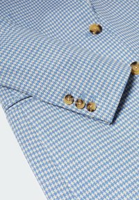 Manche de veste pied-de-poule bleu et blanc avec quatre boutons marron sur le poignet et des boutons assortis sur le corps.