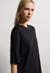 Camiseta de algodón negra con escote redondo y mangas cortas, que presenta un ajuste relajado y un sutil detalle de abertura lateral.