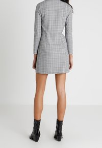 Gray, long-sleeve dress with a checkered pattern, fitted design, mid-thigh length, paired with black ankle boots. Smooth texture.