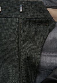 Schwarzer, strukturierter Stoff mit detaillierten Nähten, einem sichtbaren Reißverschluss und einem kontrastierenden glatten Innenfutter. Metallelemente sind vorhanden.