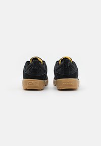 Black suede sneakers with a yellow accent on the heel tab, featuring a gum outsole, padded collar, and prominent "AIR" branding on the back.