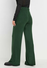 Wijde broek in een diep groene stof met een textuurafwerking. Voorzien van een comfortabele elastische tailleband en een lichte uitlopende pijp aan de zoom.