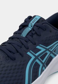 Chaussure de sport bleue avec une tige en mesh respirant, présentant un design texturé, des accents bleus et une semelle intermédiaire blanche. Les lacets sont de couleur bleu foncé.