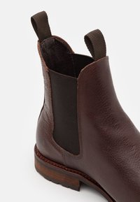 Bota Chelsea de cuero marrón con paneles laterales elásticos, superficie texturizada y un tacón de madera. Cuenta con bucles de tirón para ponerlas y quitarlas fácilmente.