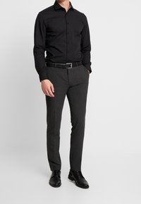 Svart långärmad skjorta med knapp-down krage, kombinerad med kolgrå byxor, svart läderbälte och svarta klämskor.