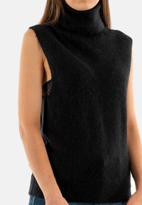 Pull en cachemire sans manches noir, fabriqué à partir d'un matériau doux et texturé. Présente une coupe décontractée avec un col montant et des ouvertures sur les côtés.