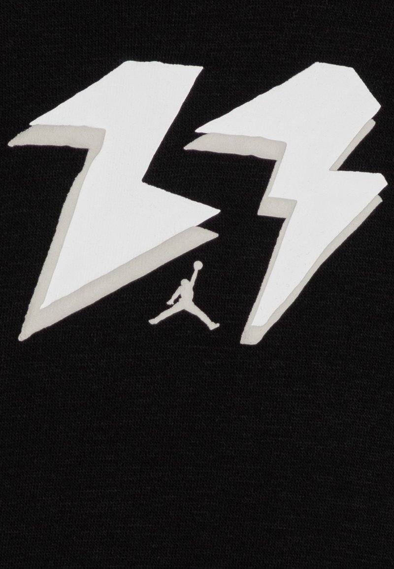 Due forme di fulmine bianche con una piccola silhouette di un giocatore di basket che salta, il tutto su uno sfondo di tessuto nero.