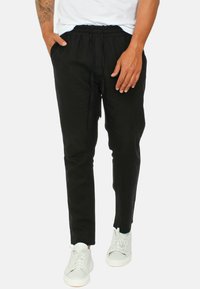 Pantaloni neri slim-fit con vita elastica e cordoncino. Realizzati in tessuto leggero, dotati di tasche laterali e una superficie liscia.
