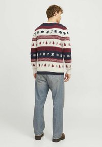 Pull en tricot à col rond, avec un motif décoratif en bleu marine, rouge et crème, illustrant des thèmes de vacances. Associé à un jean en denim clair.