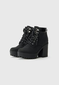 Bottines à plateforme noires avec des talons épais, œillets de lacets renforcés et un col rembourré sur un fond clair.