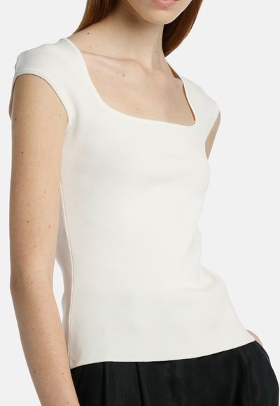 Top bianco lavorato a maglia con scollatura quadrata e maniche corte. Il tessuto ha una consistenza liscia e un design attillato, abbinato a una gonna nera.