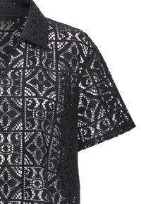 Chemise noire à manches courtes en dentelle avec des motifs floraux géométriques et un col, présentant un design ajouré complexe.