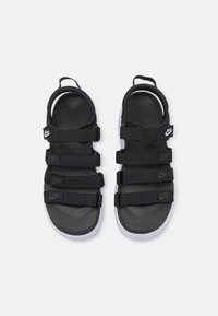 Sandales noires Nike avec plusieurs sangles noires et logos. Dotées d'un semelle texturée et d'une semelle en caoutchouc blanche. Conçues pour le confort et le soutien.