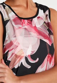 Blouse sans manches avec un imprimé floral dans des teintes de rose et de blanc sur un fond noir, dotée d'un col rond et de détails froncés aux épaules.