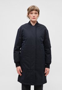 Dlhá tmavomodrá bunda stojacím golierom, predným zapínaním, bočnými vreckami a rebrovanými manžetami. Vyrobená z hladkého, odolného materiálu.