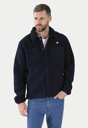 Giacca in pile navy con colletto, due tasche sul petto, chiusura con bottoni e un piccolo logo sul lato sinistro. Tessuto morbido e strutturato.