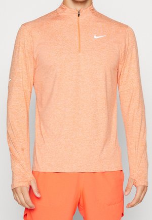 Uomo che indossa una maglietta sportiva Nike a maniche lunghe di un arancione chiaro e pantaloni corti arancioni brillanti con aperture per il pollice sulle maniche.