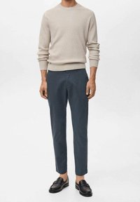 Béžový žebrovaný svetr v kombinaci s tmavě modrými zúženými kalhotami a černými mokasínami. Souprava má jednoduchý a čistý design.