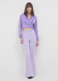 Lila satinierte Wickelbluse mit langen Ärmeln und Federakzenten; kombiniert mit hoch taillierten, auslaufenden lavendelfarbenen Hosen.