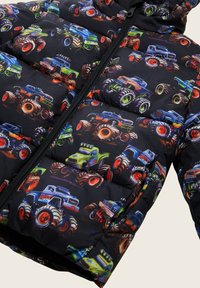 Giacca a vento con sfondo nero e fantasie di monster truck colorati. Il materiale è lucido con sezioni imbottite e chiusura a zip.