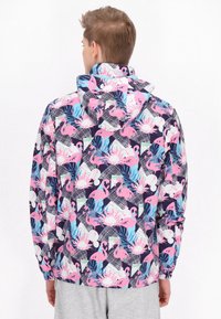 Jachetă ușoară colorată cu glugă, având un imprimeu vibrant cu flamingo și flori pe un fundal întunecat, și manșete elastice.