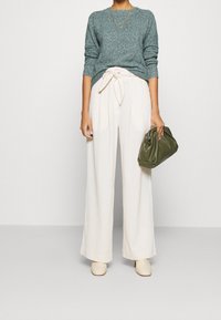 Vaaleanvihreä neulepaita, kermanväriset leveät housut, joissa on solmittava vyötärö, vaaleat korkokengät ja tummanvihreä käsilaukku. Suuret tekstuurit ja rento istuvuus.