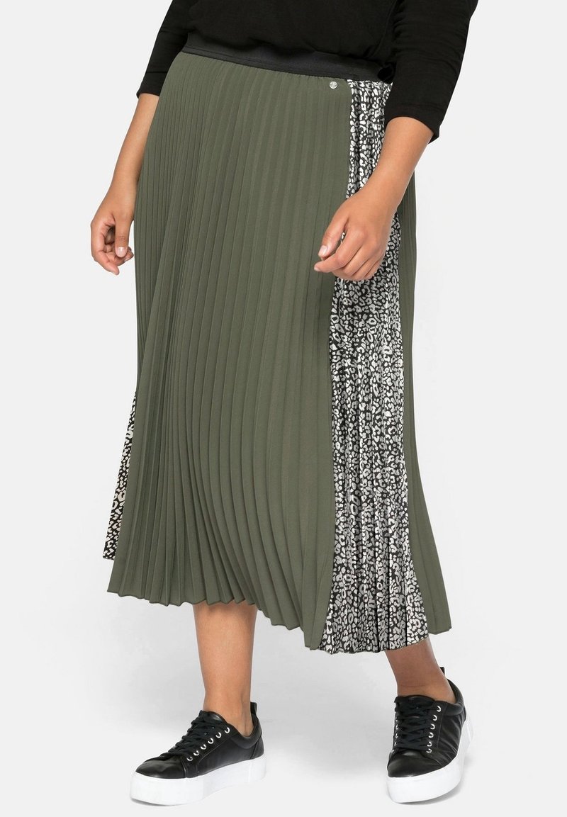 Jupe midi plissée vert olive avec une taille élastique noire. Présence sur le côté d'un panneau imprimé animal noir et blanc. Stylisée avec des baskets noires.