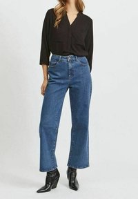 Maglietta nera a maniche lunghe con scollatura a V, abbinata a jeans blu a vita alta e gamba dritta, e stivaletti neri con punta.