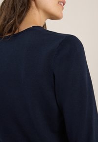 Granatowy sweter z dzianiny z okrągłym dekoltem, gładką fakturą i rękawami raglanowymi, prezentujący zbliżenie na plecy.