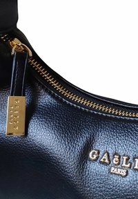 Borsa a tracolla nera in pelle con superficie strutturata, zip dorata e un'etichetta decorativa con la scritta "GAËLLE PARIS" in lettere dorate.