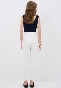 Marineblauwe geribbelde tanktop gecombineerd met hoge witte broeken. De broeken hebben eenTailored fit en zakken, aangevuld met zwarte schoenen.