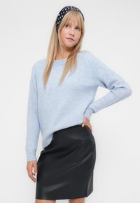 Světle modrý pletený svetr s uvolněným střihem a dlouhými rukávy, kombinovaný s černou koženou sukní, která má hladkou texturu a elegantní siluetu.