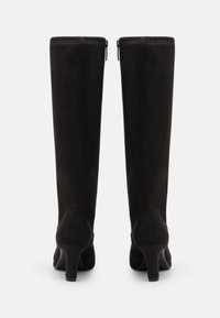 Bottes noires en suede jusqu'aux genoux avec un design épuré, dotées d'un talon effilé et d'une fermeture éclair à l'arrière. Texture lisse et style minimaliste.