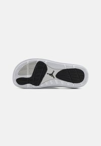 Shoe sole features a white base with a textured black rubber pattern, highlighting a central logo and distinct tread design.