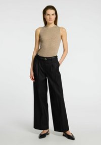 Beige ribbet tanktop uden ærmer, kombineret med højtaljede sorte bukser med vidde, der har et bælte med guldfarvet accent. Sorte flade sko fuldender outfittet.
