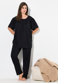 Ensemble de vêtements de détente noir composé d'un haut ample à manches courtes et de pantalons fuselés. Fabriqué en tissu doux avec une texture lisse. Comprend une couverture en tricot beige douillette.