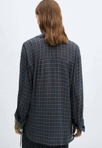 Chemise à manches longues en flanelle à carreaux bleu foncé, vert et marron. Caractérisée par un empiècement au dos, une coupe ample et des poignets boutonnés avec des accents au niveau des poignets.